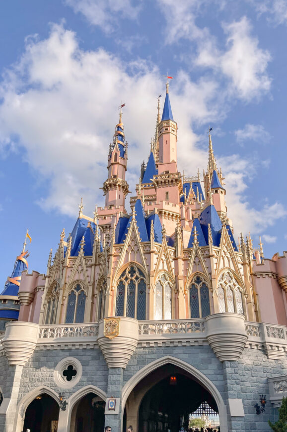 Cinderella Castle at Disney World, a magical sight for families, including those visiting Disney World with autistic kids, features blue and gold spires, pink walls, and intricate architectural details under a partly cloudy blue sky.