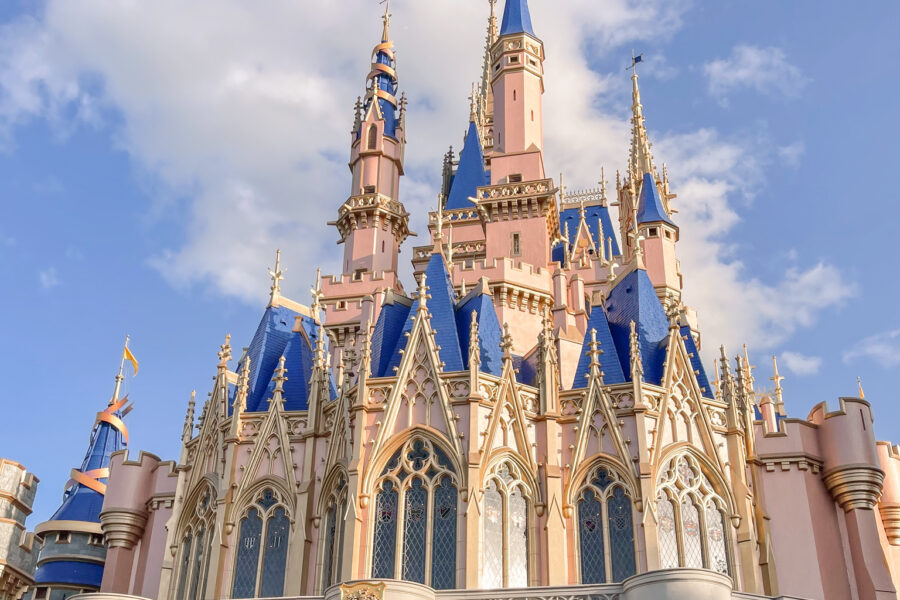 Cinderella Castle at Disney World, a magical sight for families, including those visiting Disney World with autistic kids, features blue and gold spires, pink walls, and intricate architectural details under a partly cloudy blue sky.